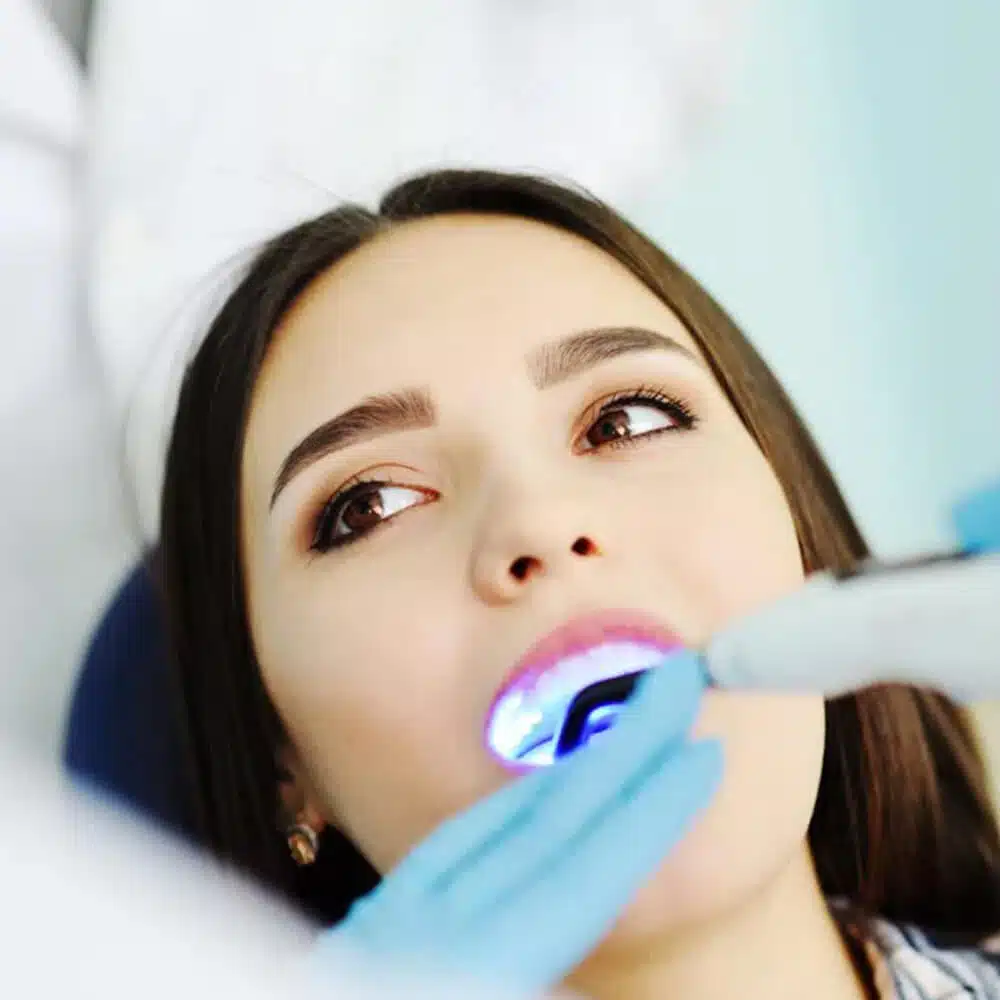 Woman receiving dental examination with blue dental mirror in clinical setting.