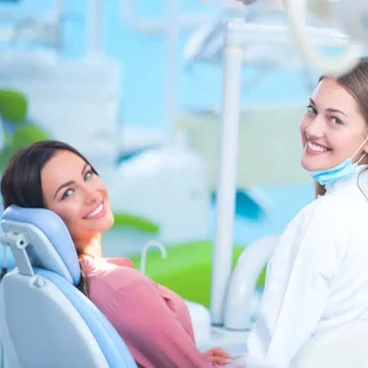Dentist in white coat smiling at patient in dental chair during appointment.