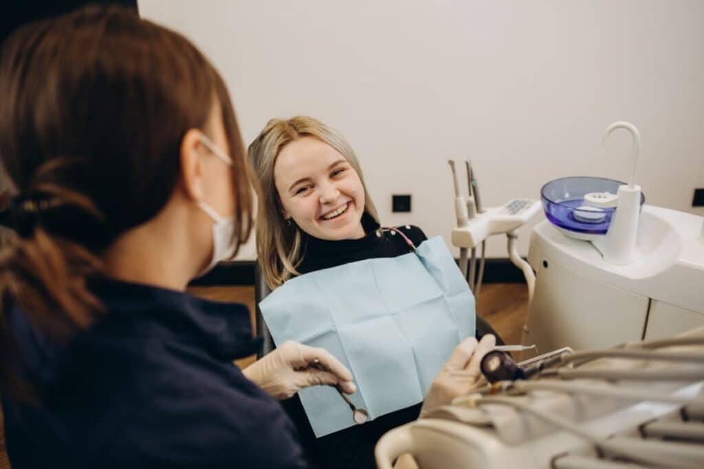 Dental hygienist placing bib on patient in treatment room during dental appointment.
